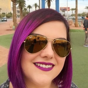 Porträtfoto von Jessica Hassler mit lila Haaren und gold verspiegelter Sonnenbrille, fotografiert vor dem Las Vegas Willkommensschild