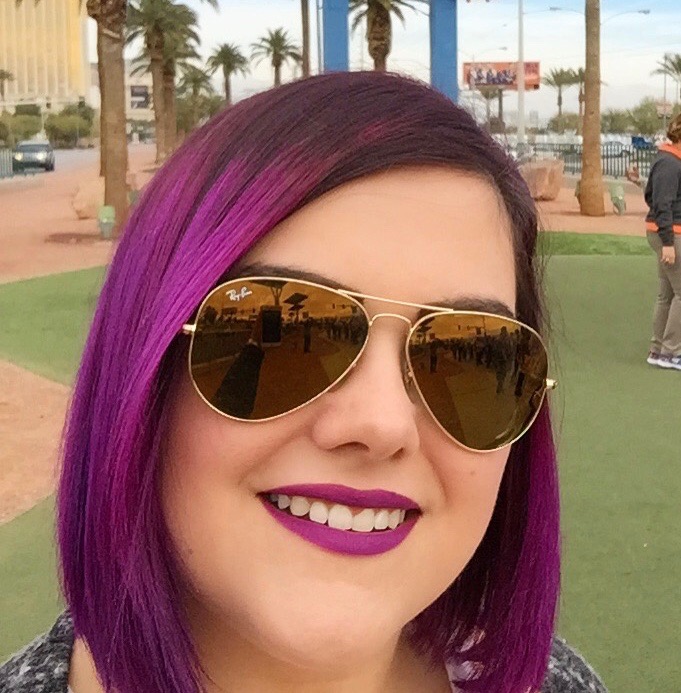 Porträtfoto von Jessica Hassler mit lila Haaren und gold verspiegelter Sonnenbrille, fotografiert vor dem Las Vegas Willkommensschild