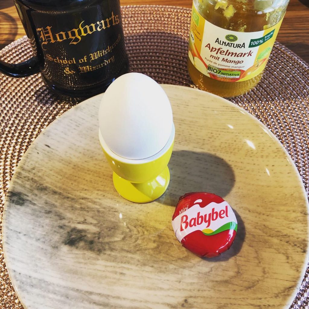 Frühstücks-Ei, Babybel auf einem Teller mit Kaffeetasse und Fruchtpüree