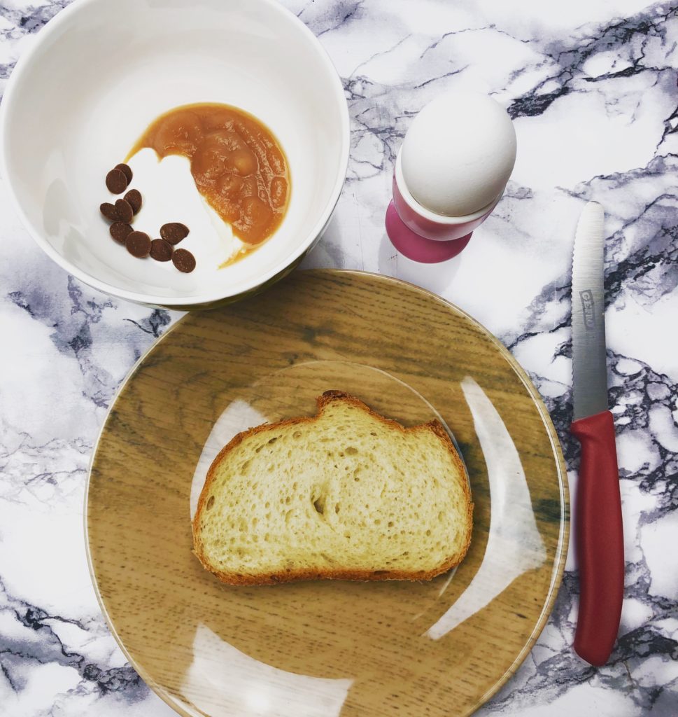 Scheibe Brot auf einem Teller, Frühstücksei und Quark in einer Schale mit Fruchtpüree